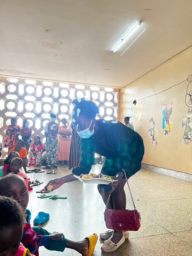 A masked volunteer carrying a plate of food across the ward to children waiting on the floor
