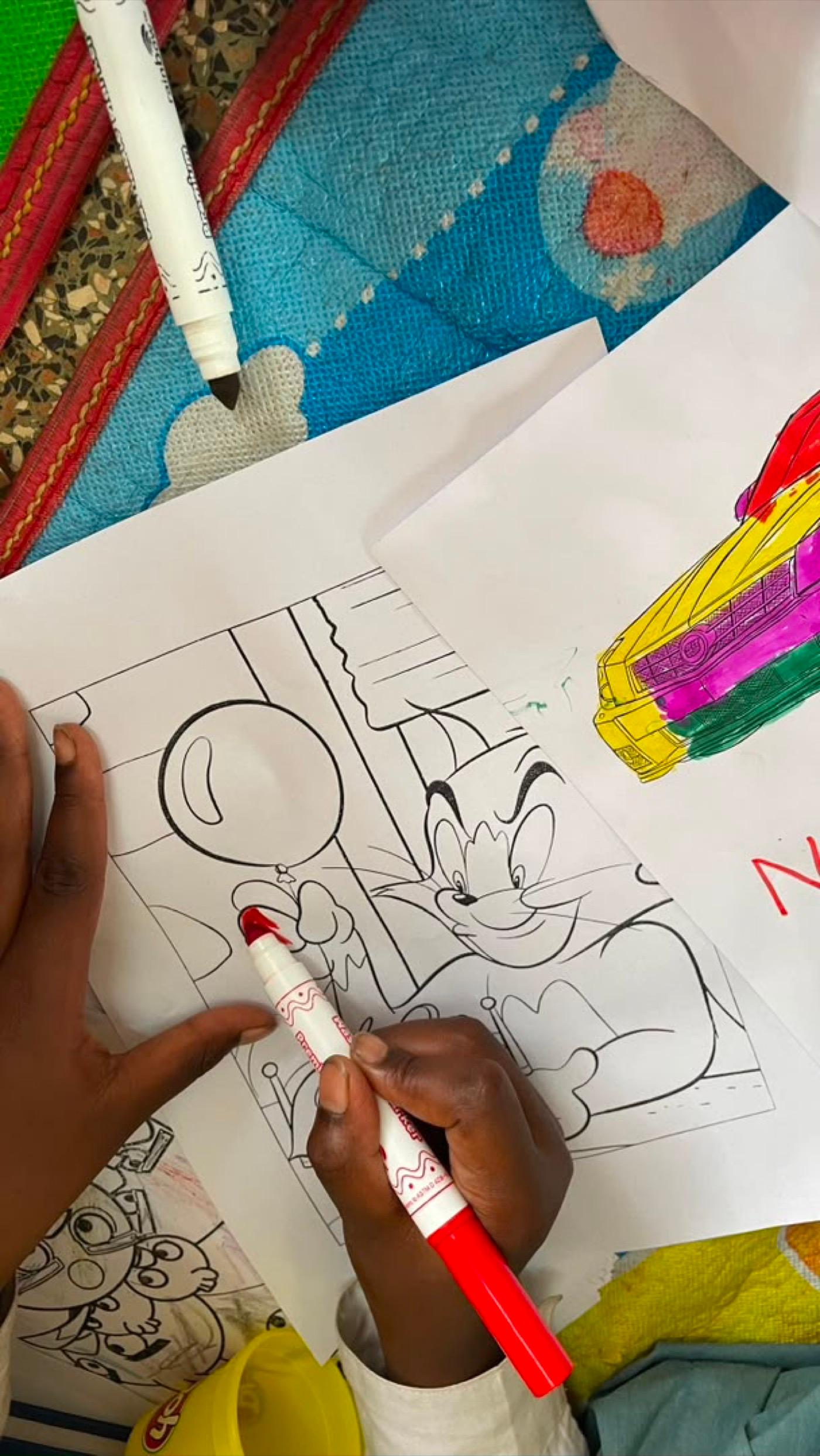 A child coating a cartoon outline in red felt-tip, other finished pages spread around them