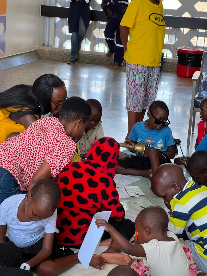 Children and volunteers sitting together on the ward floor, drawing on sheets of paper