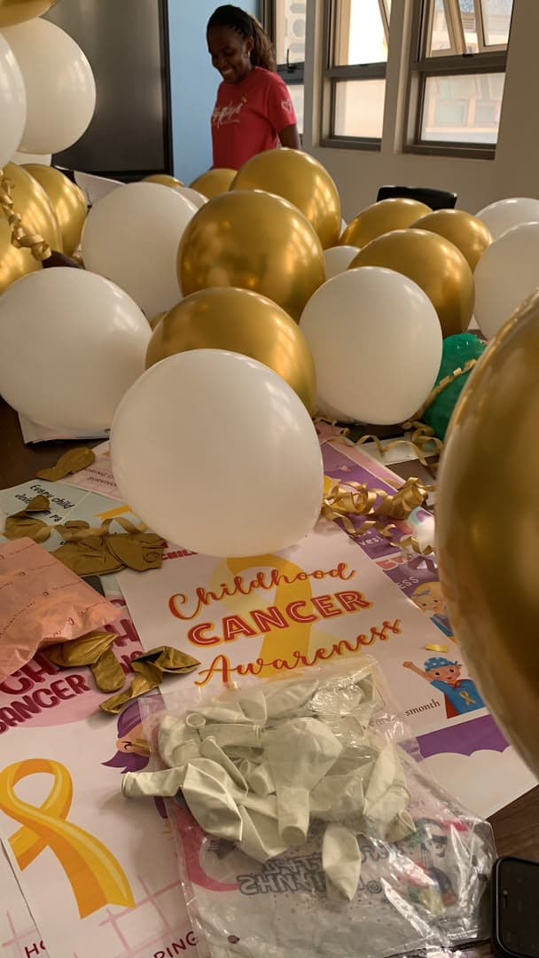 Gold and white balloons and Childhood Cancer Awareness cards laid out while the room is decorated