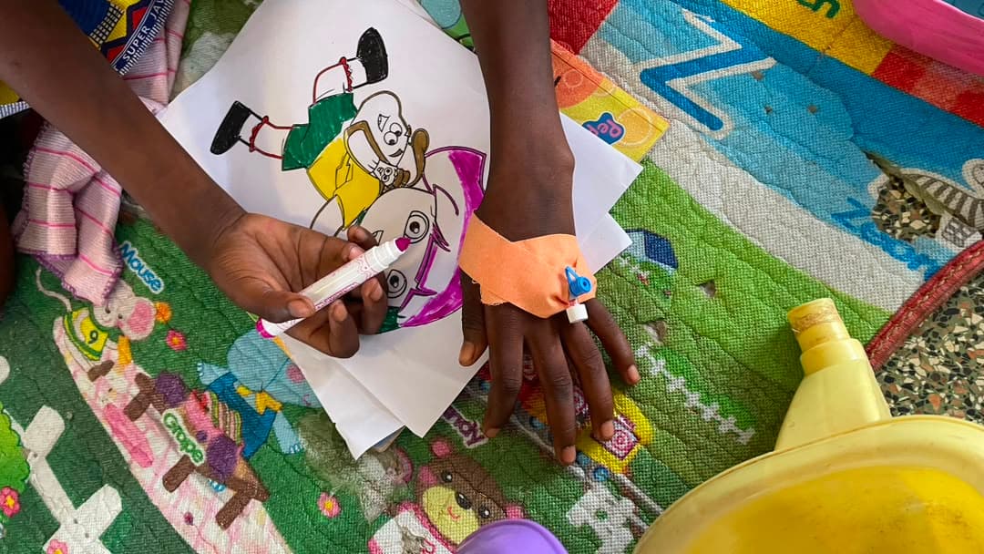 A child’s hands colouring a cartoon page with felt-tip pens on a patterned play mat