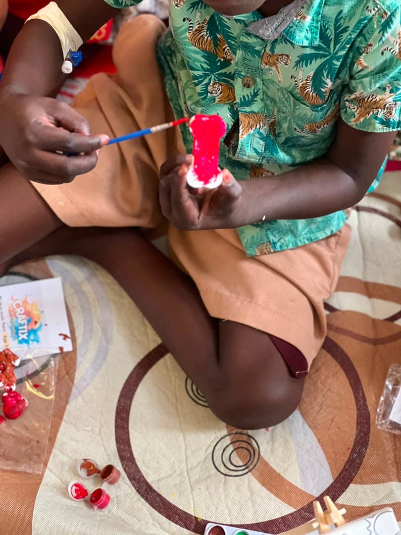 A child sitting cross-legged on a mat, painting a small figure with a brush