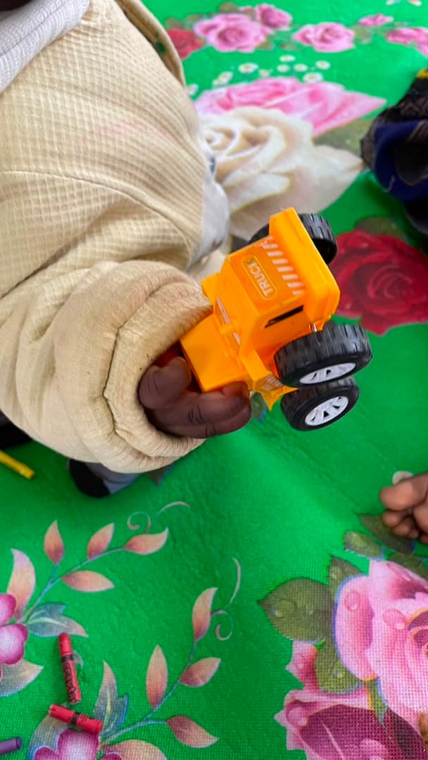 A young child holding a yellow toy truck on a green flowered blanket