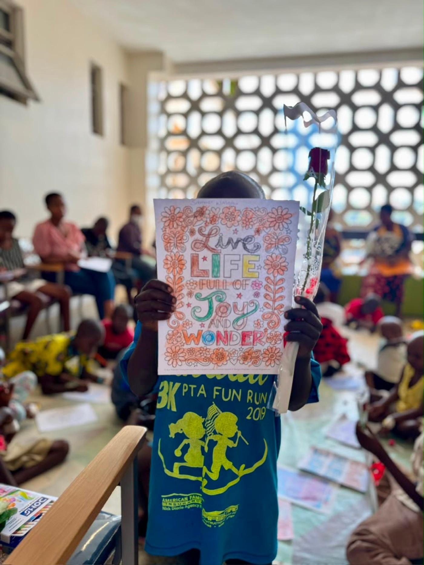 A child on the ward holding up a coloured page reading Live life full of joy and wonder
