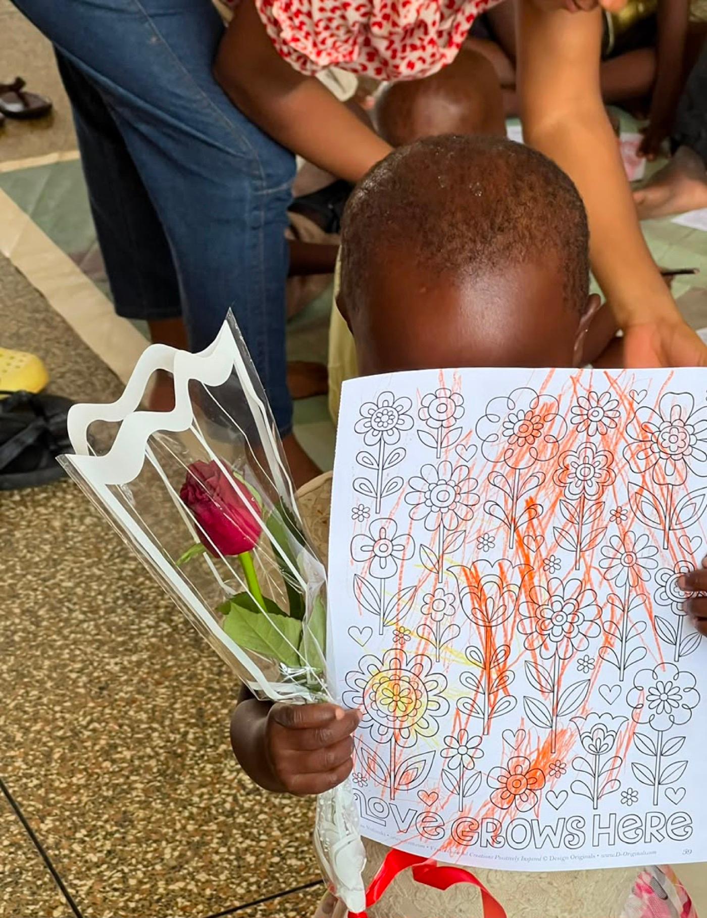 A child holding a flower and a colouring page captioned Love grows here